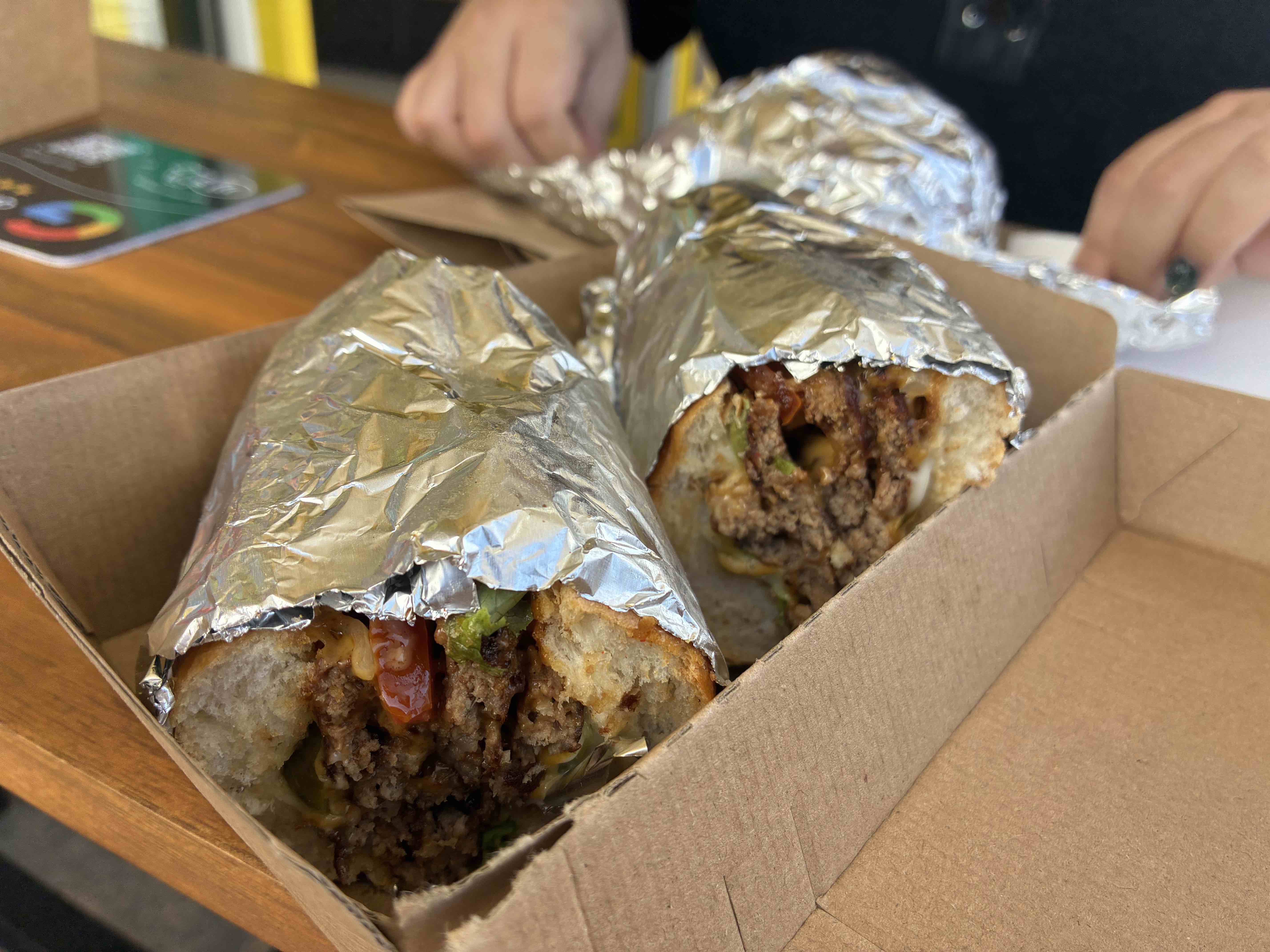 A chopped cheese sandwich wrapped in alfoil. The contents are visible from where the sandwich has been cut in half and turned to the camera: Melted american cheese, chopped burger patties, and a bit of lettuce and tomato.