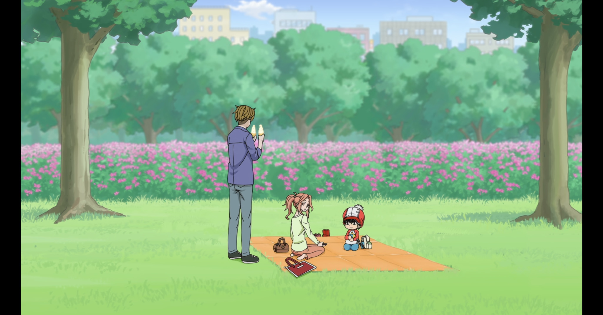 A young man (Karino) holding two soft serve cones standing over a young woman (Mizuki) and small child (Kotaro) sitting on a picnic blanket in a park.