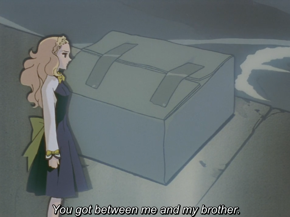 Nanami, in a dark dress with a yellow bow, stands glaring at a large grey box with two pieces of duct tape loosely holding it shut, in a gloomy setting. The subtitle reads "You got between me and my brother."
