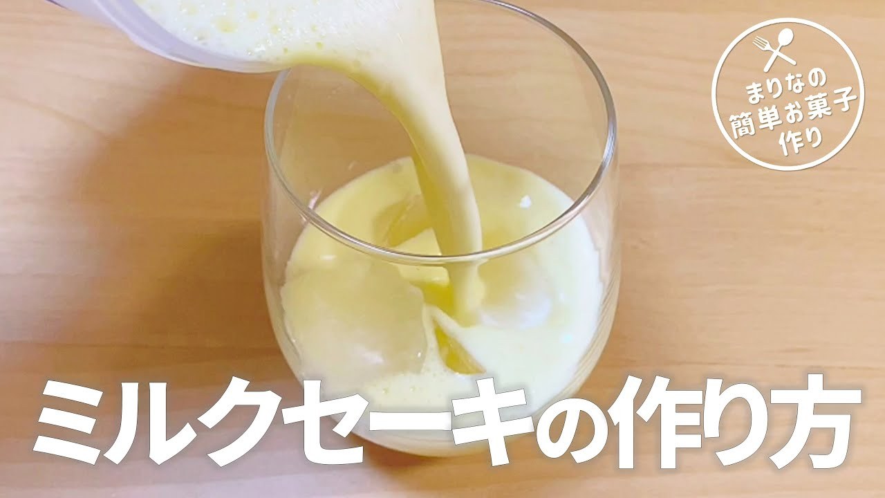 A thumbnail from a Japanese recipe video: a thick pale-yellow drink being poured into a glass over ice. Large text reads “ミルクセーキの作り方” (How to make mirukusēki), and a round logo reads “まりなの簡単お菓子作り”.