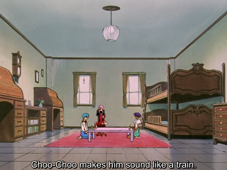 A wide shot of a dorm room with bunk beds, where Miki and Anthy kneel at a low pink table while Utena sits in a chair behind them. The subtitle reads “Choo-Choo makes him sound like a train.”
