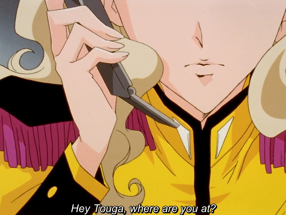 A close-up of the lower half of a face: a blonde girl in a yellow uniform with pink fringed epaulettes holds a phone to her ear. The subtitle reads "Hey Touga, where are you at?"