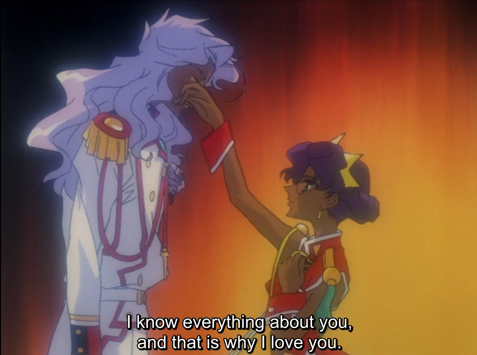 Anthy reaches up and touches Akio’s face as he leans down towards her, against a fiery red-orange background. The subtitle reads “I know everything about you, and that is why I love you.”